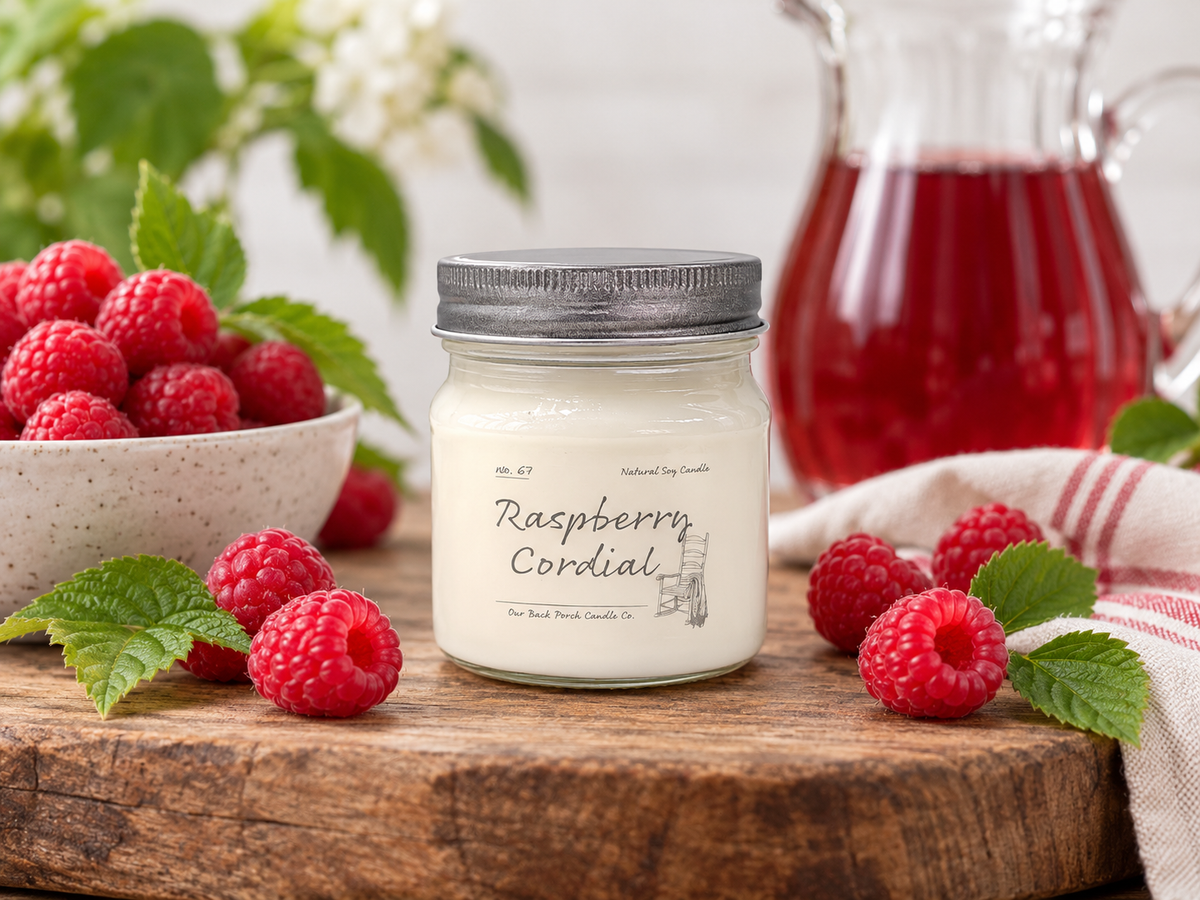 Back Porch Candle Co Raspberry Cordial 8 oz soy candle styled with raspberries and raspberry cordial in a warm rustic setting.