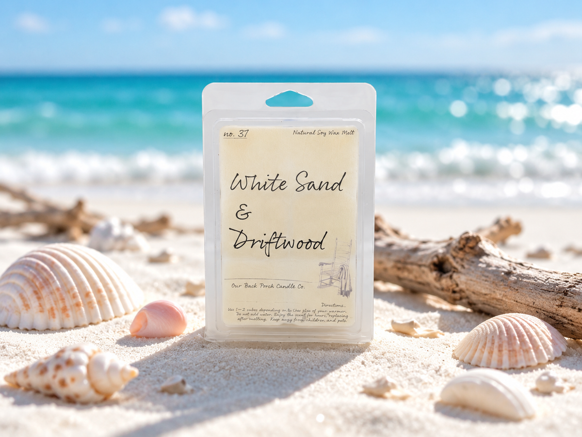 Back Porch Candle Co White Sand & Driftwood 6 oz soy wax melt on white sand with seashells and driftwood in a bright coastal setting.