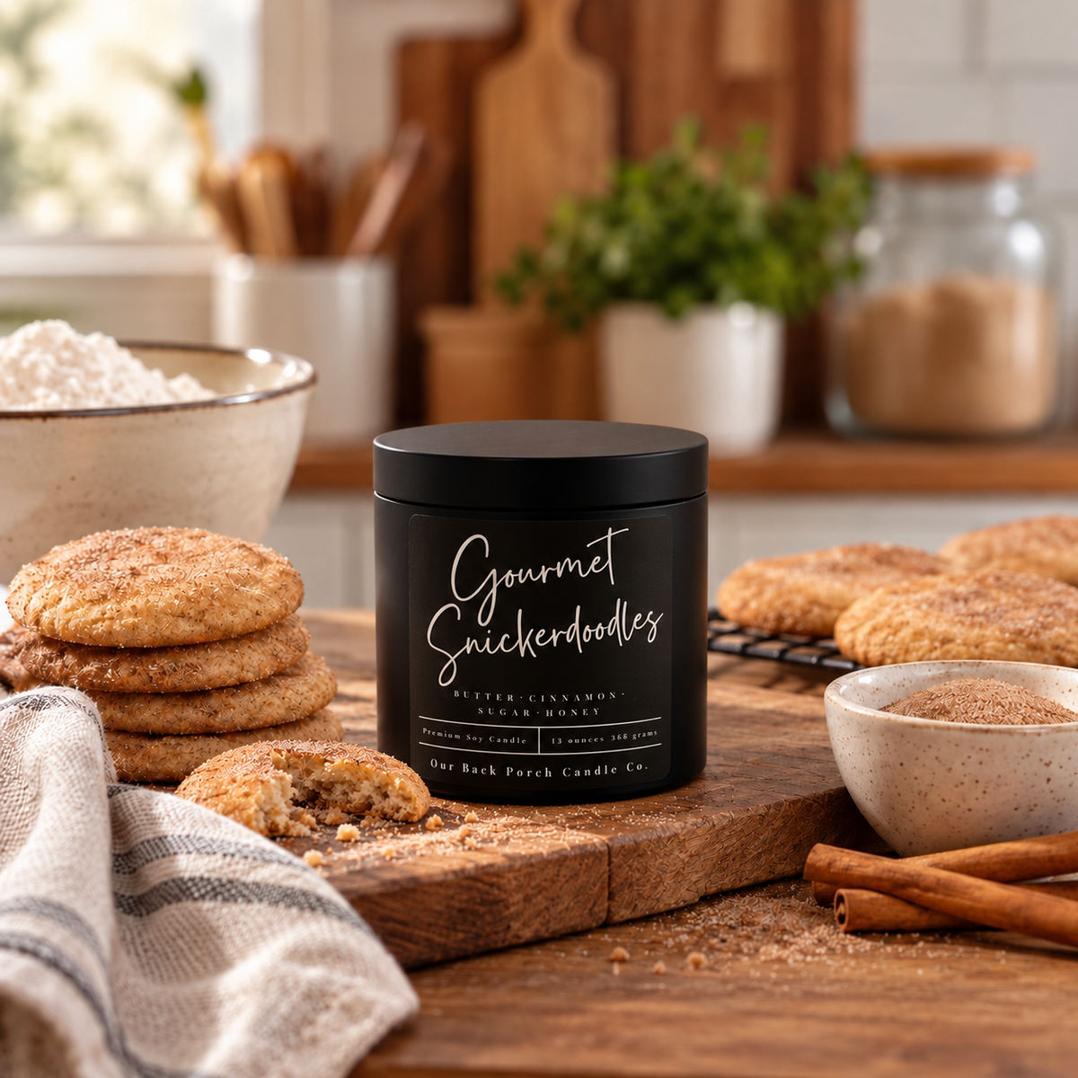 Gourmet Snickerdoodles 16oz Black Tin soy candle by Back Porch Candle Co. with cinnamon sugar cookies and baking ingredients on a warm farmhouse kitchen countertop.